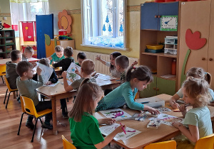 Dzieci z grupy przy stolikach kolorują obrazek z dinozaurem.